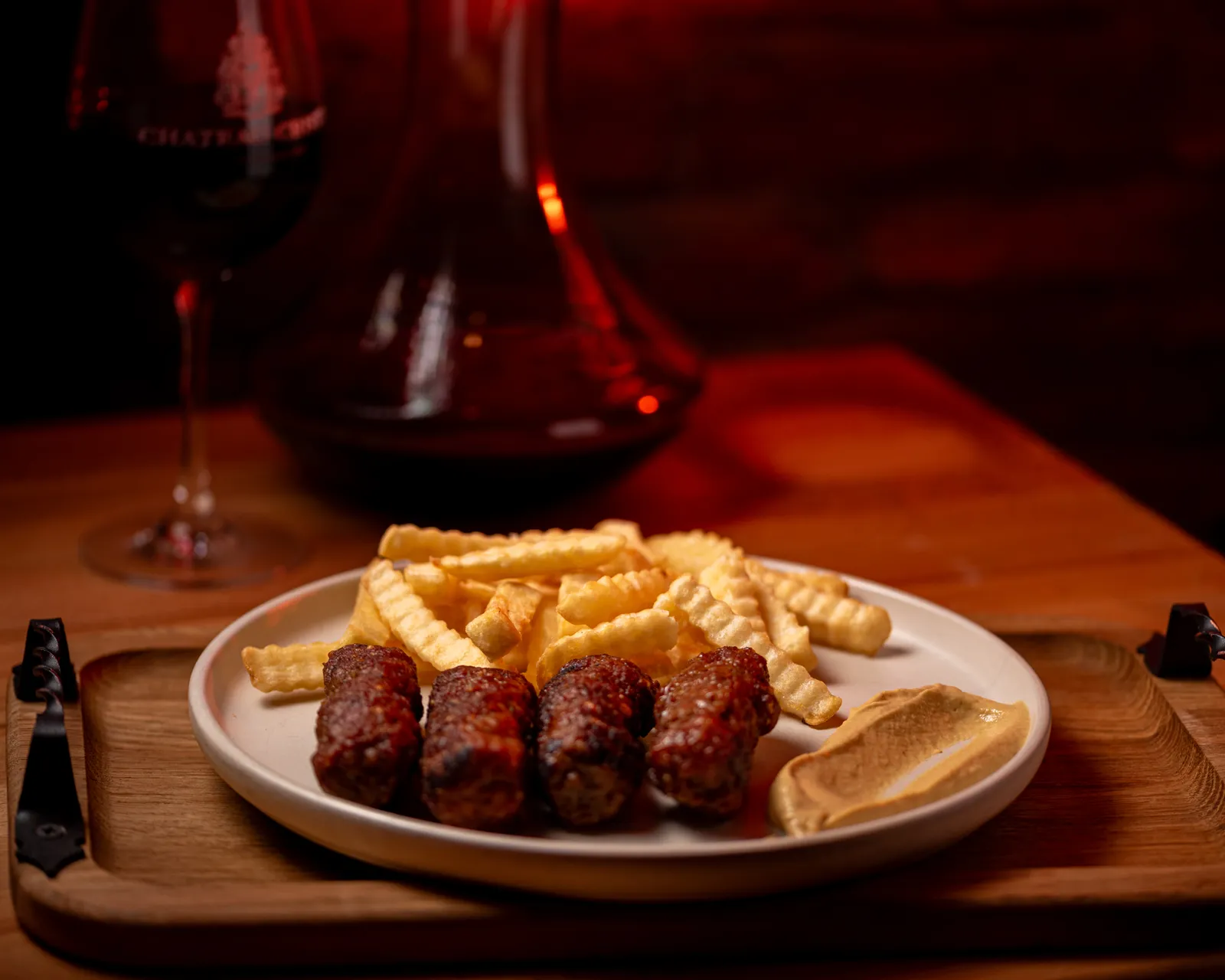 Mici de casă cu cartofi prăjiți și muștar, lângă un pahar de vin
